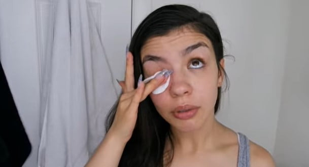 How to naturally darken eyelashes: woman thoroughly cleaning her eyelashes with a cotton pad